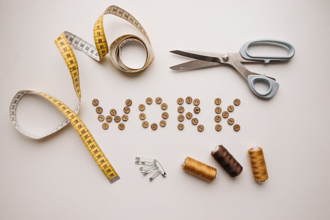 Flat lay of sewing tools and 'work' spelled out with buttons on a white background.